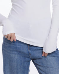 A close-up of a person wearing a white long-sleeve top and blue jeans, with both hands resting in the front pockets of the jeans against a plain white background.