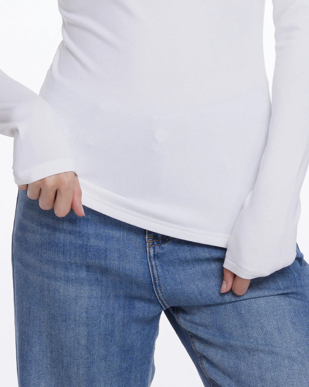 A close-up of a person wearing a white long-sleeve top and blue jeans, with both hands resting in the front pockets of the jeans against a plain white background.