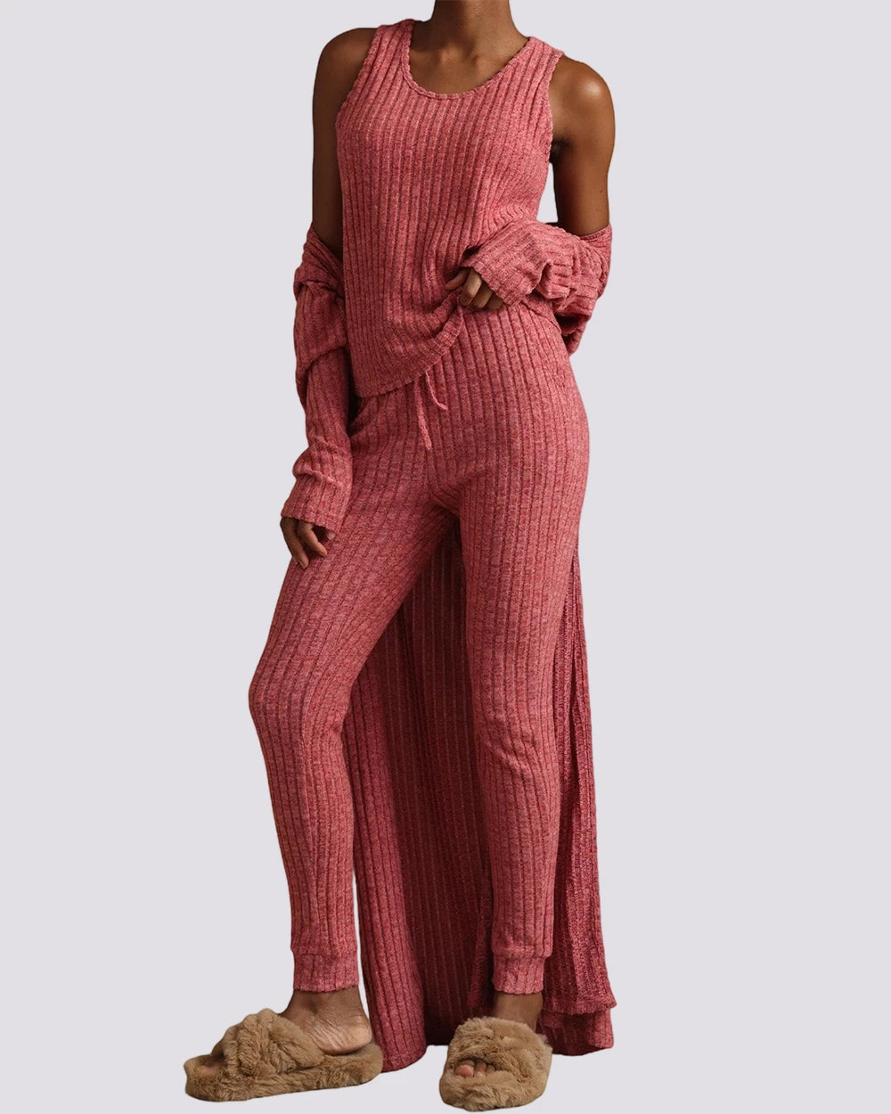Person wearing a pink ribbed lounge set with slippers on a gray background