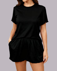 A woman wearing a black short-sleeve t-shirt and matching black shorts, shown from the neck down against a solid gray background.
