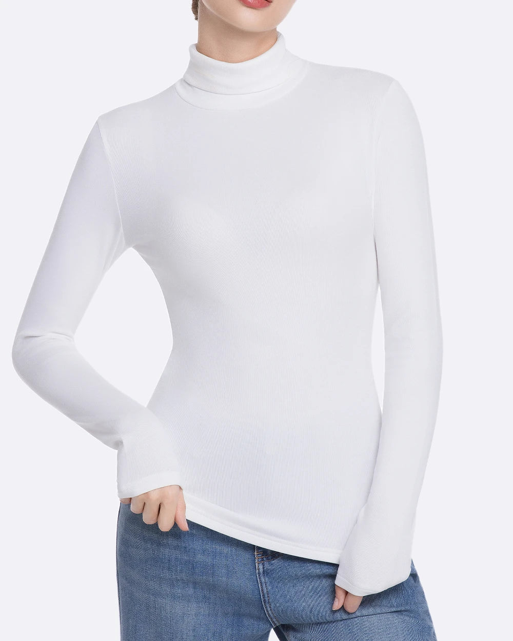 A woman wearing a fitted white long-sleeve mock neck turtleneck top with blue jeans, shown from the neck down against a light gray studio background.