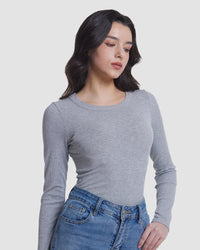 A woman wearing a fitted long-sleeve crewneck top in heather gray, paired with blue jeans, photographed against a plain light gray studio background.