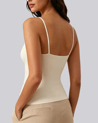 A woman shown from the back wearing a fitted spaghetti-strap camisole top in a warm off-white/cream color, paired with beige pants, against a solid light gray background.