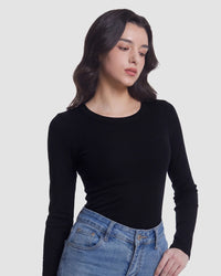 A woman wearing a fitted black long-sleeve crewneck top and blue jeans, photographed against a plain light gray studio background.