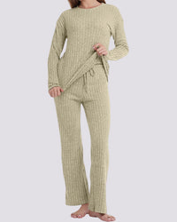 A woman modeling a ribbed knit two-piece loungewear set in a light sage green color, featuring a long-sleeve top and matching wide-leg pants, against a solid light gray background.