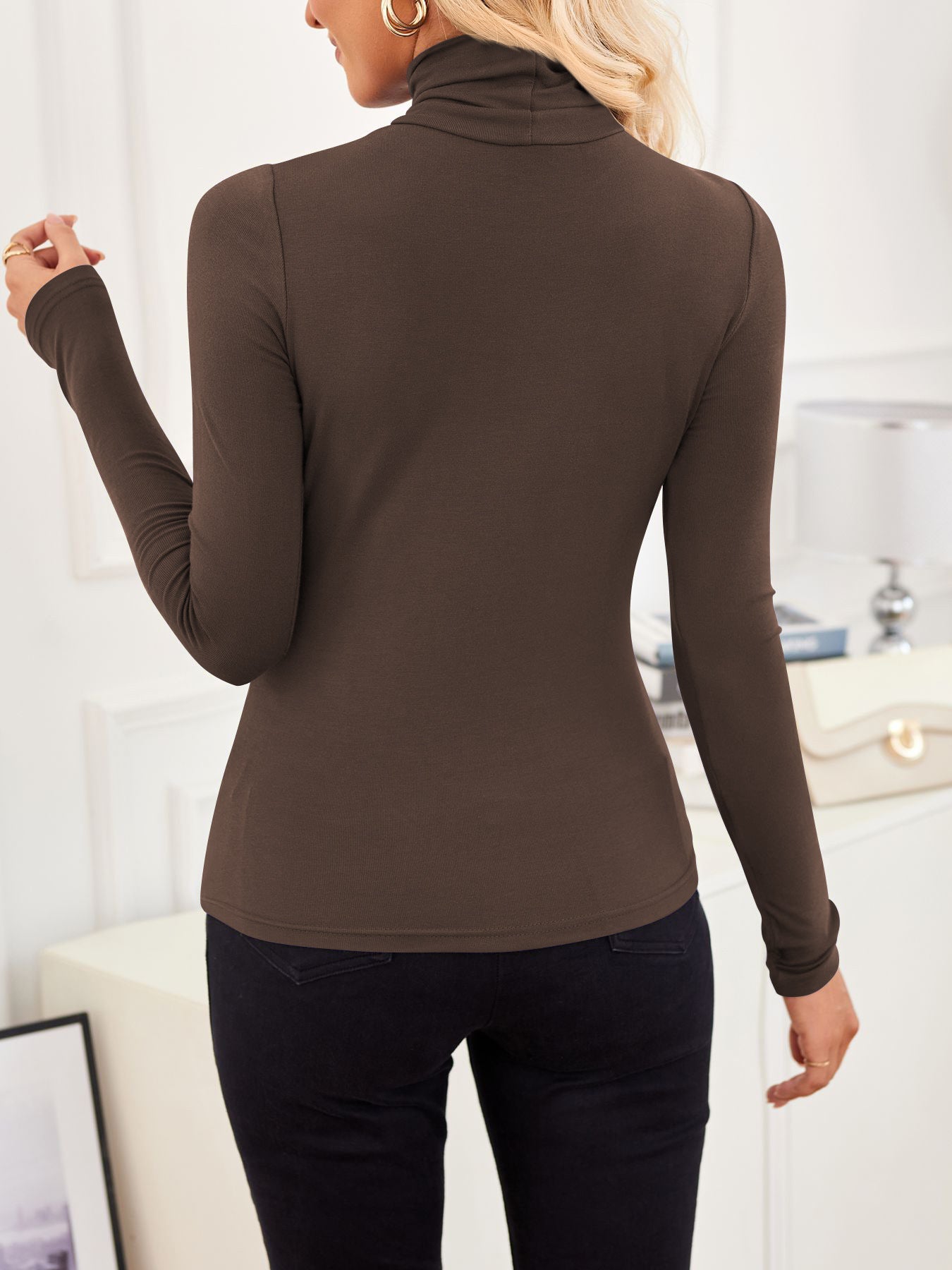 Back view of VRCÔMFY mocha brown turtleneck top with sculpted silhouette, styled with tailored black trousers and sand beige bag featuring gilded lock-clasp | Architectural minimalism and refined urban elegance in a curated lifestyle setting