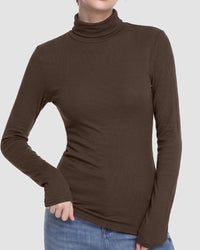 A woman wearing a fitted, ribbed long-sleeve turtleneck top in dark brown, paired with blue jeans, shown against a plain light gray background.