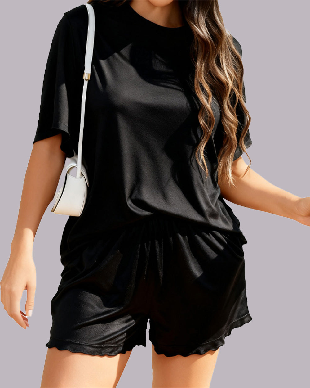 A woman wearing a black short-sleeve t-shirt and matching black shorts with a scalloped hem, carrying a small white shoulder bag against a solid gray background.