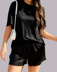 A woman wearing a black short-sleeve t-shirt and matching black shorts with a scalloped hem, carrying a small white shoulder bag against a solid gray background.