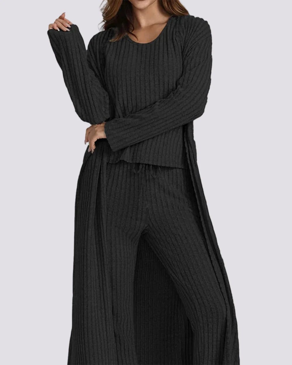 Woman wearing a black ribbed sweater and pants set on a gray background