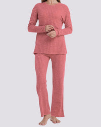 A woman modeling a two-piece ribbed knit pajama set in a dusty rose pink color, featuring a long-sleeve top and matching pants, against a solid light gray background.