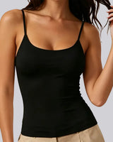 A woman wearing a black spaghetti-strap camisole tank top paired with beige pants, shown from the shoulders to the hips against a light gray studio background.