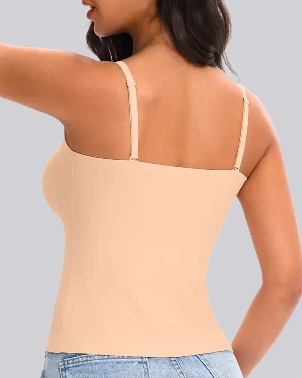 A woman shown from the back wearing a beige/nude camisole tank top with thin shoulder straps and a shapewear-style body contour, paired with light blue jeans against a plain light gray studio background.