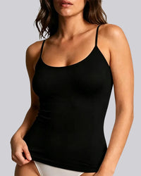 A woman wearing a black spaghetti-strap camisole tank top against a solid light gray background.
