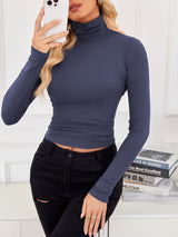 VRCÔMFY twilight blue cropped turtleneck top with contour-defining fit, styled with artfully distressed black jeans against a curated literary backdrop | Urban intellectual edge and architectural minimalism for the modern cosmopolitan woman
