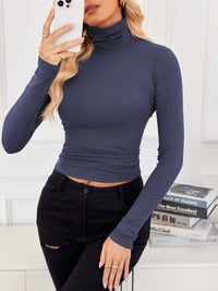 VRCÔMFY twilight blue cropped turtleneck top with contour-defining fit, styled with artfully distressed black jeans against a curated literary backdrop | Urban intellectual edge and architectural minimalism for the modern cosmopolitan woman