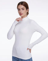 A woman modeling a fitted white long-sleeve mock neck top against a plain light gray studio background.