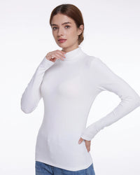 A woman modeling a fitted white long-sleeve mock neck top against a plain light gray studio background.