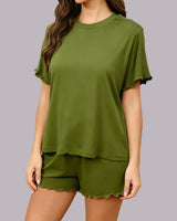 A woman wearing an olive green two-piece lounge set with a short-sleeve top and matching shorts, both featuring scalloped edges, shown against a solid gray background.
