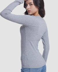 A woman wearing a fitted light gray long-sleeve top, shown from the back and side against a plain light gray studio background.