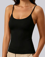 A woman wearing a black spaghetti-strap tank top and beige pants, shown from the neck down against a solid gray background.