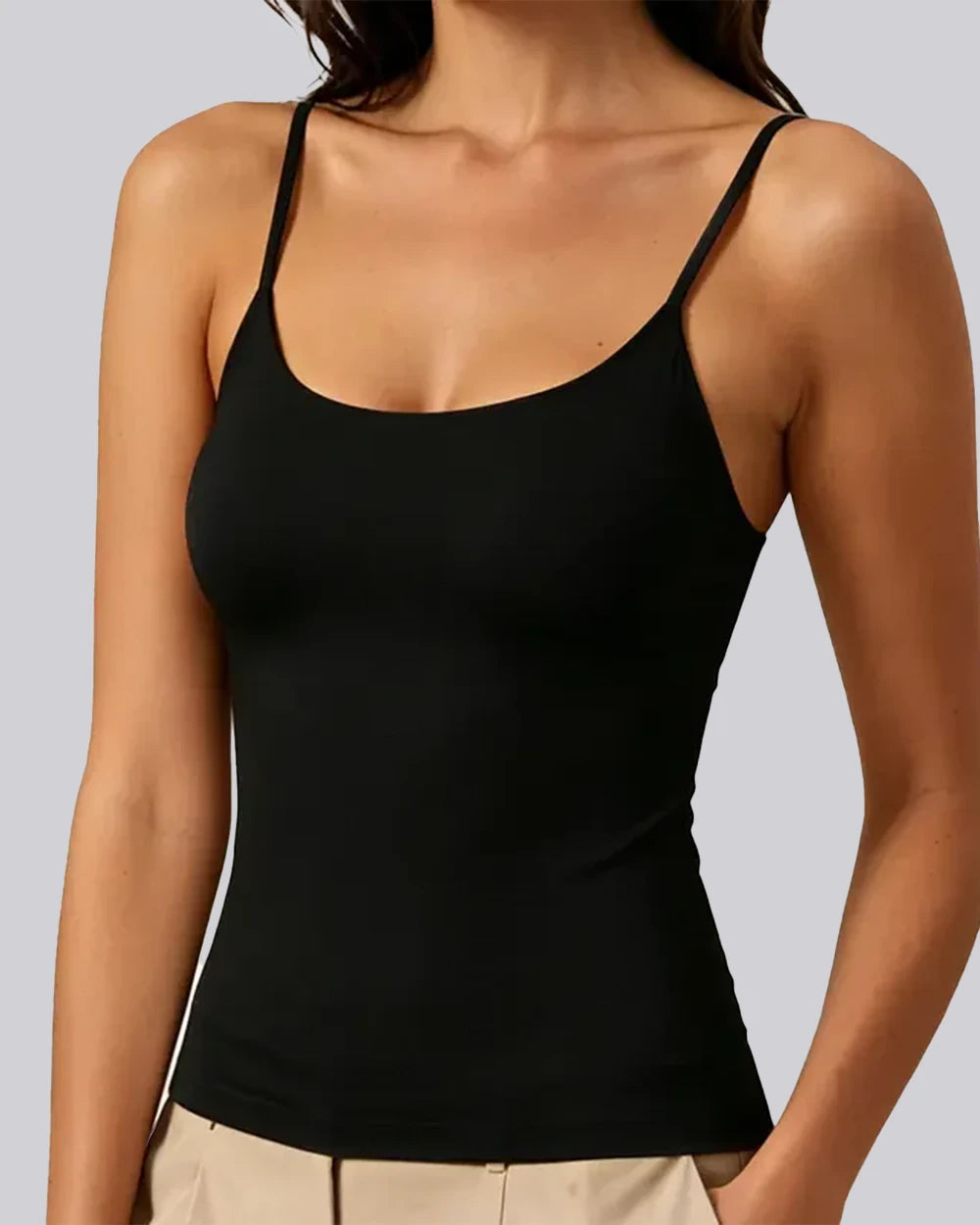 A woman wearing a black spaghetti-strap tank top and beige pants, shown from the neck down against a solid gray background.