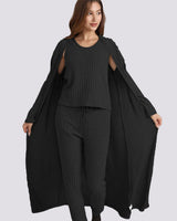 A woman modeling a black ribbed knit three-piece outfit consisting of a sleeveless top with shoulder cutouts, matching wide-leg pants, and a long open-front cardigan, shown against a solid light gray background.
