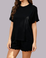 A woman wearing a black short-sleeve t-shirt and matching black shorts with scalloped hems, shown against a solid gray studio background.