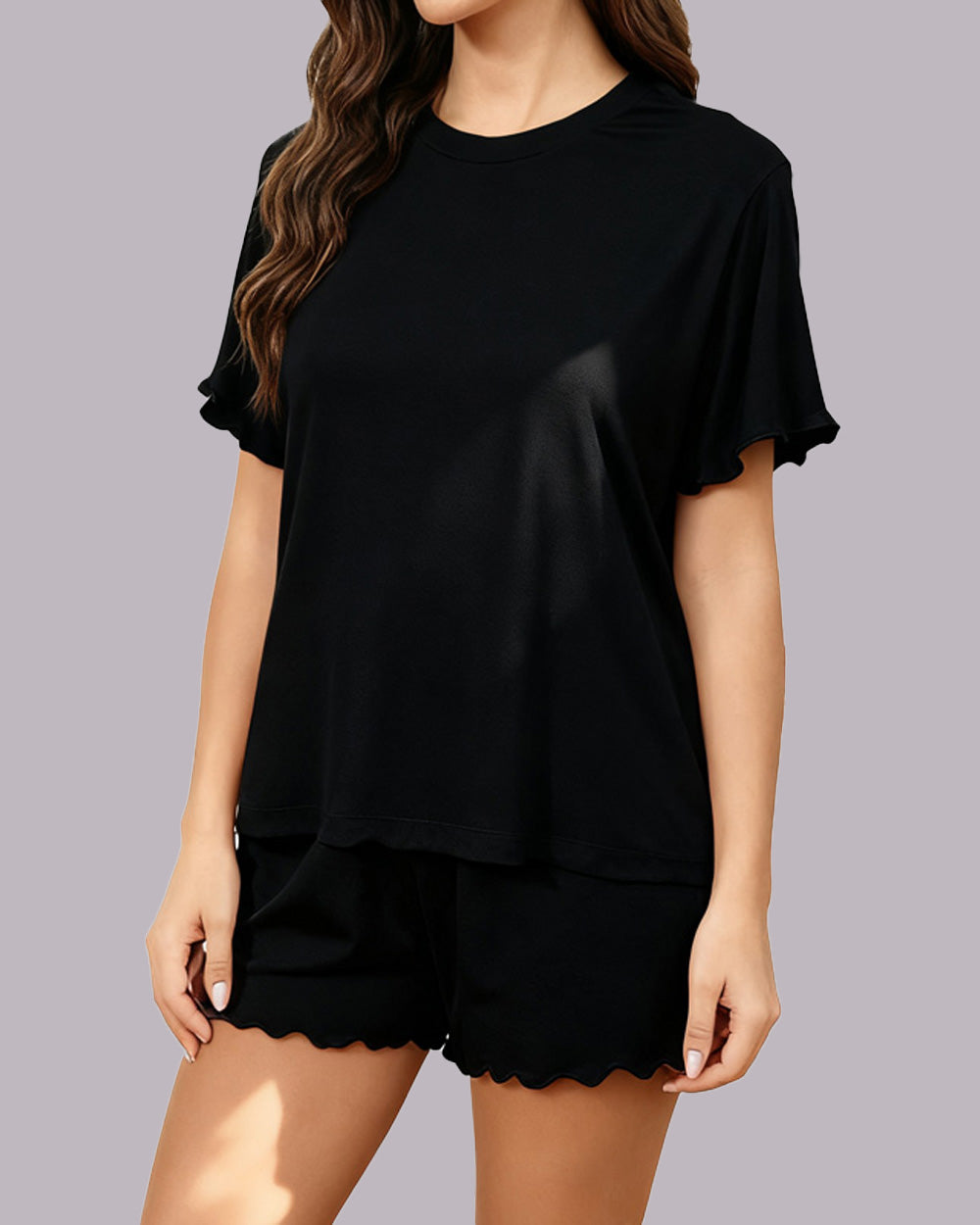 A woman wearing a black short-sleeve t-shirt and matching black shorts with scalloped hems, shown against a solid gray studio background.