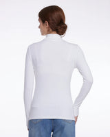 A woman shown from the back wearing a fitted white long-sleeve mock-neck top and blue jeans against a plain white studio background.