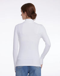 A woman shown from the back wearing a fitted white long-sleeve mock-neck top and blue jeans against a plain white studio background.