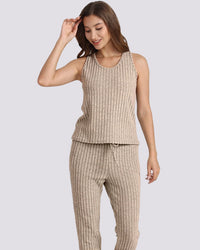 A woman modeling a matching ribbed knit lounge set consisting of a sleeveless tank top and drawstring pants in a warm beige color, set against a solid light gray background.