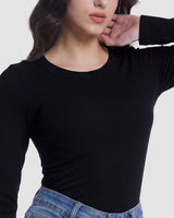 A woman wearing a fitted black long-sleeve ribbed top and blue jeans, cropped from the nose down against a light gray studio background.