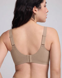 Rear view of a woman wearing a beige wireless bra with wide adjustable shoulder straps and a smooth seamless back design, featuring a center closure and supportive fit against a light gray studio background.