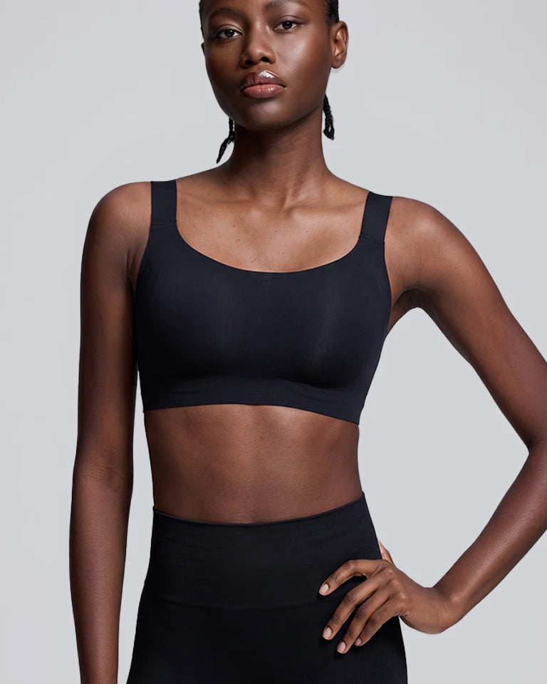A woman modeling a black scoop-neck athletic sports bra against a solid light gray background.