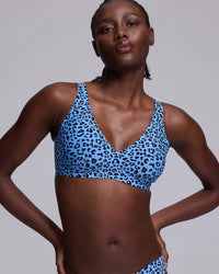 A woman modeling a blue and black leopard print bikini top against a plain light gray studio background.