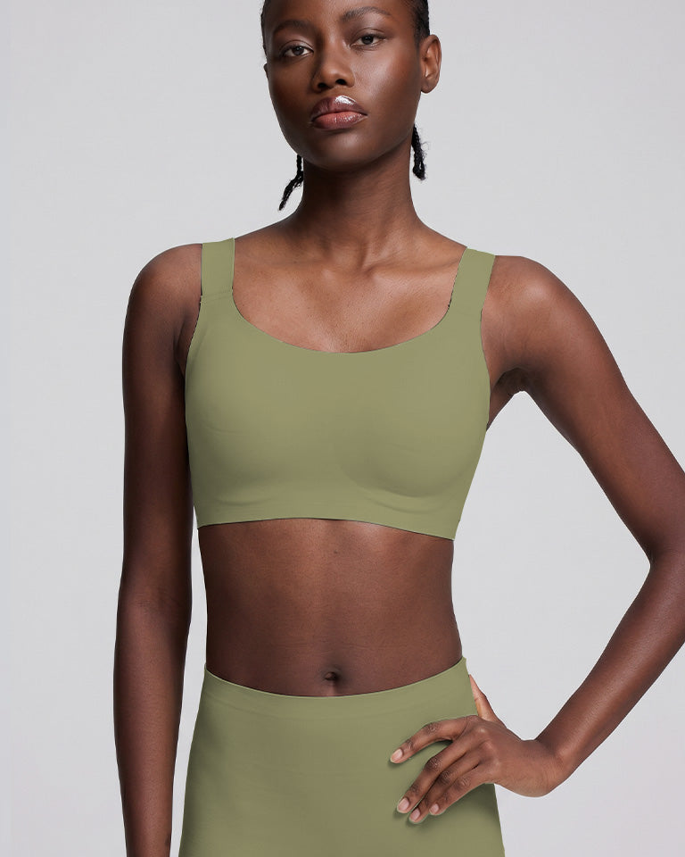 A model wearing a solid sage green sports bra and matching high-waisted leggings against a light gray studio background.