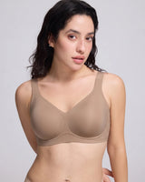 A woman modeling a seamless,VRCOMFY wireless bra in a light taupe-beige color, shown from the chest down against a solid light gray background.
