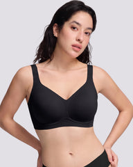 A woman modeling a vrcomfy black wireless bra against a light gray studio background.