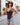 A woman wearing a dark brown bodysuit and denim shorts stands on a cobblestone street holding an ice cream cone.