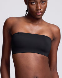 A close-up of a model wearing a black strapless bandeau tube top against a light gray background.