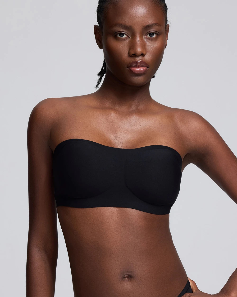 A woman modeling a black strapless bandeau-style bra against a light gray studio background.