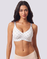 A woman modeling a white underwire bra with VRCOMFY white polka dots and gray shoulder straps, paired with beige underwear, against a solid light gray background.