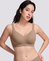 A woman modeling a seamless, VRCOMFY wireless bra in a solid taupe-beige color, shown from the chest down against a light gray studio background.