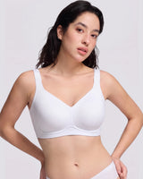 A woman modeling a white wireless bra with a V-neckline and wide shoulder straps, photographed against a light gray studio background.