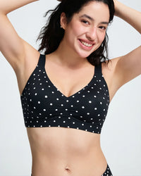 A woman wearing a black V-neck bralette with white polka dots, posing against a light gray studio background.