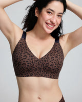 A woman wearing a brown leopard-print bralette with dark navy underwire and shoulder straps, shown from the chest up against a light gray studio background.