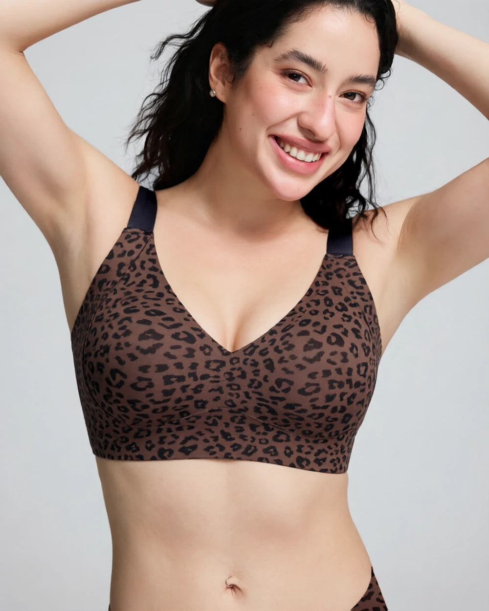 A woman wearing a brown leopard-print bralette with dark navy underwire and shoulder straps, shown from the chest up against a light gray studio background.