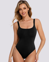 A woman modeling a black scoop-neck one-piece swimsuit against a solid light gray background.