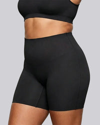 A close-up of a model wearing black high-waisted athletic shorts and a matching black sports bra against a solid gray background.